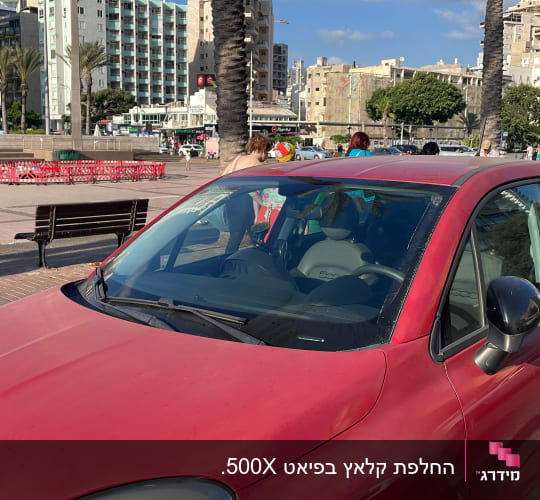מכונית אדומה חונה ליד מדרכה עם עצי דקל ברקע